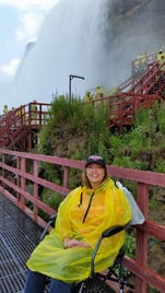 A woman sits in the Travelite Transport Chair in front of Niagra Falls